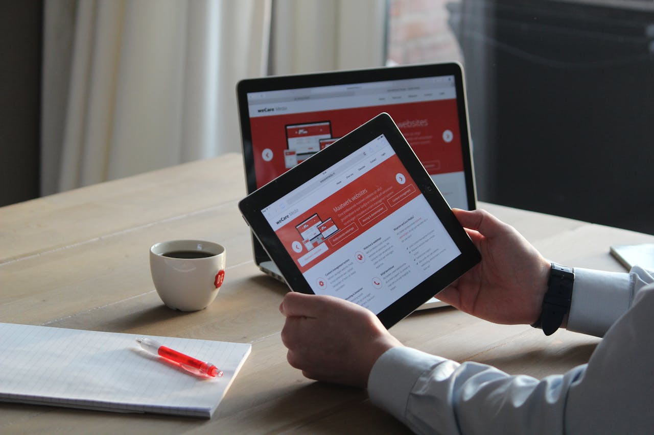 services-01 Business professional using a tablet and laptop with a hot drink, focusing on digital content review.